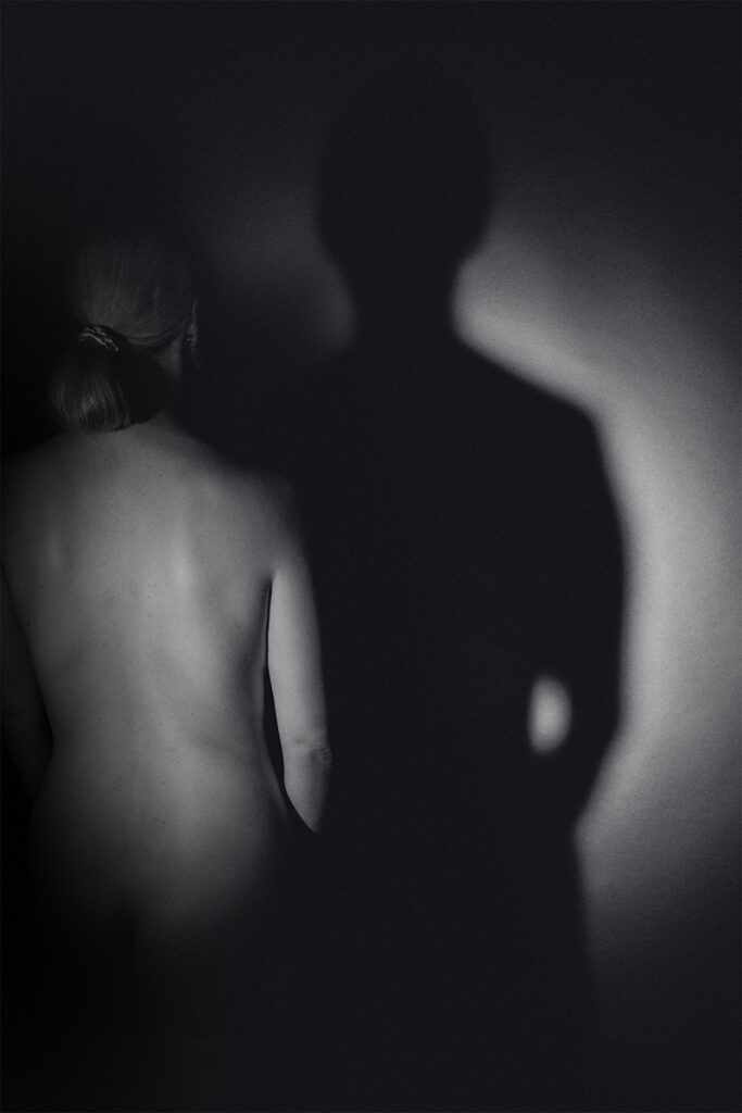 Schwarzweißfotografie eines weiblichen Körpers im Schatten, reduziert ausgeleuchtet